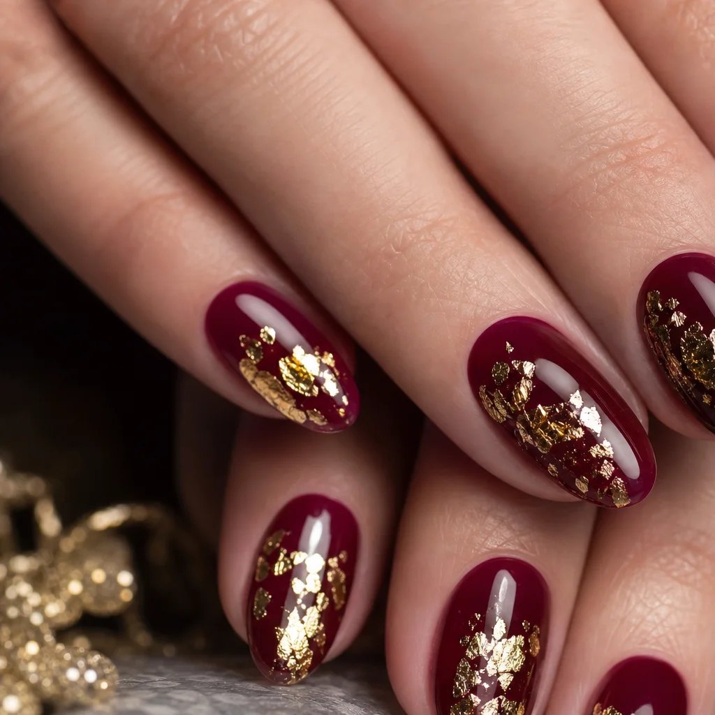 Gold foil flake nail art with metallic accents on a deep burgundy gel base