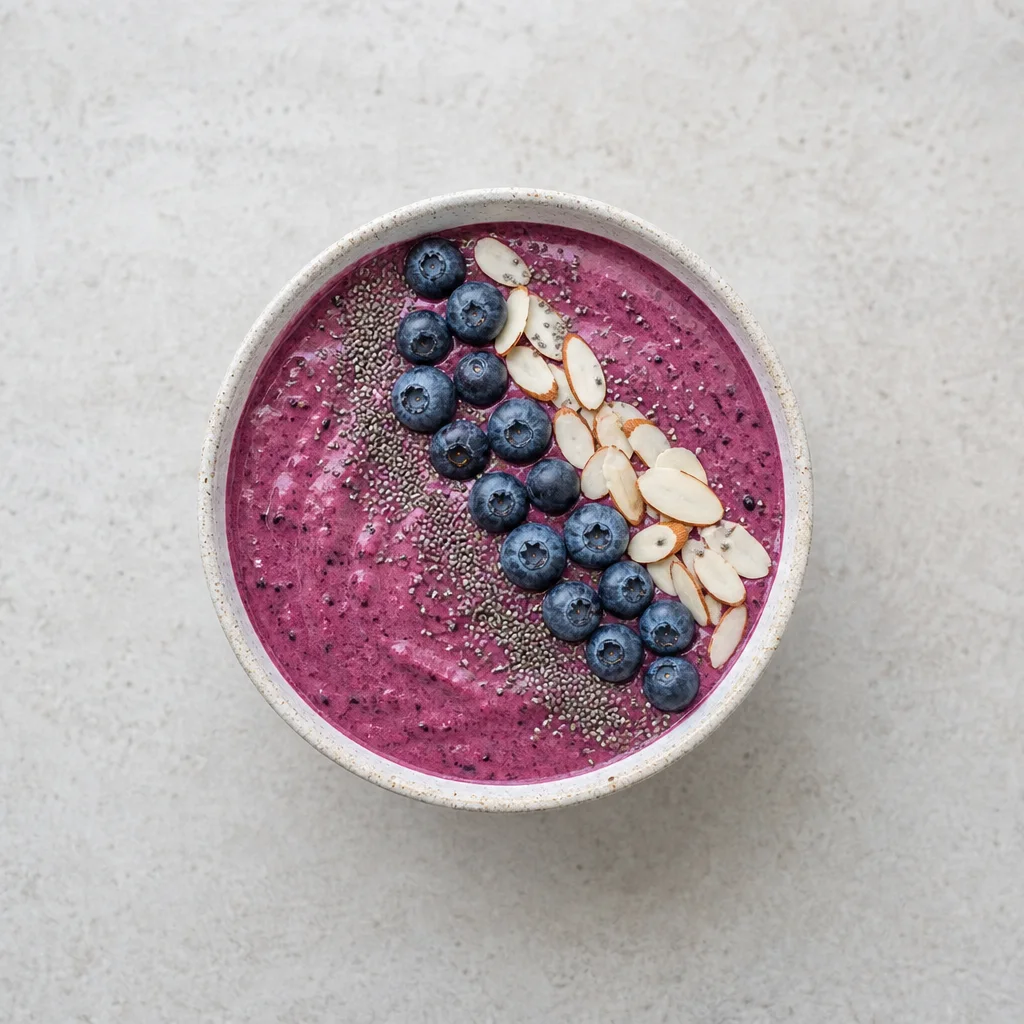 Thick berry smoothie bowl topped with chia seeds sliced almonds and fresh blueberries
