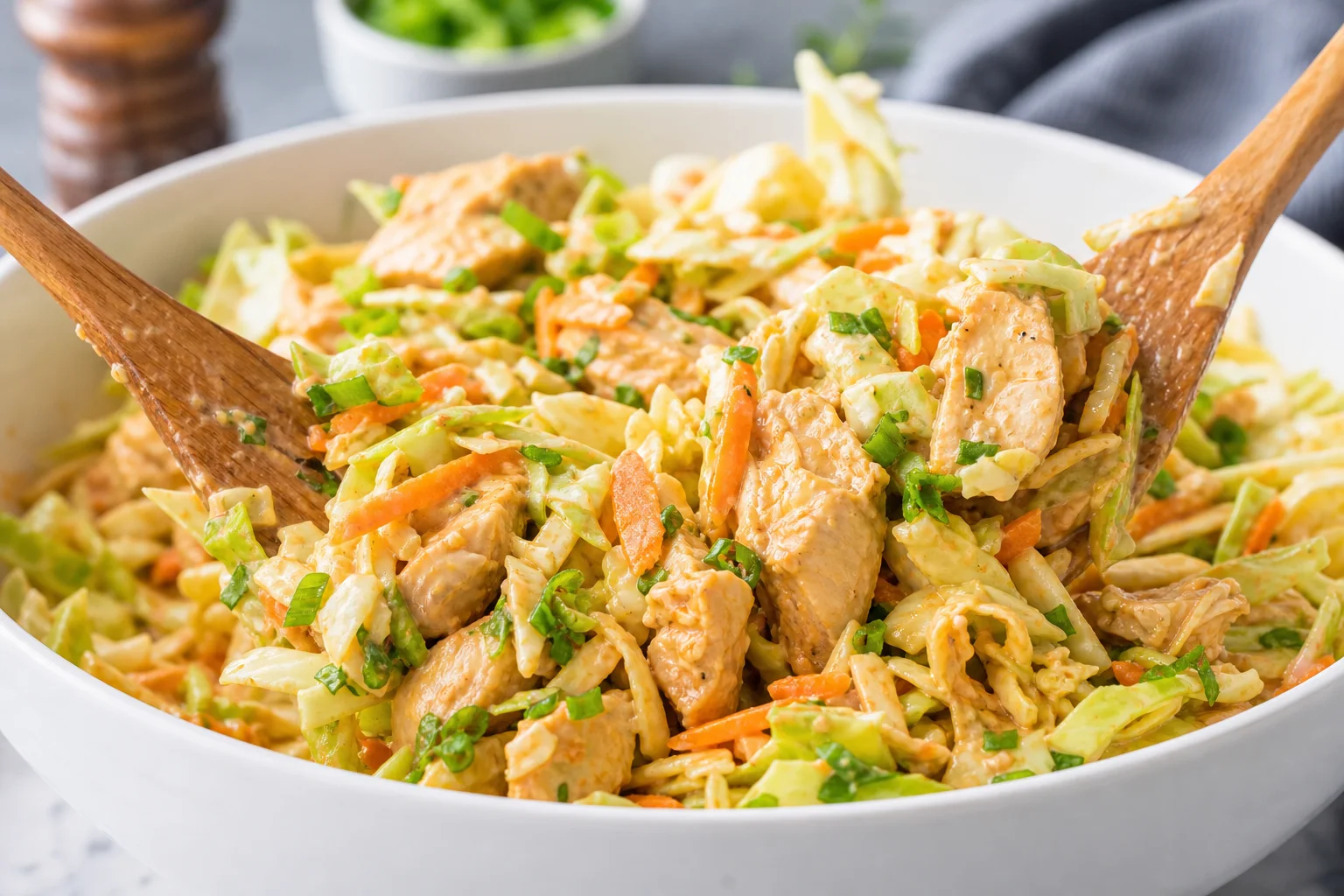 Bang bang chicken salad tossed in a large white bowl with creamy spicy dressing and shredded vegetables