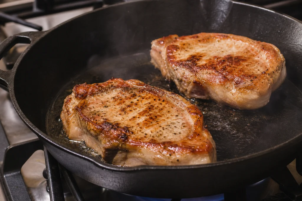 Bone-in pork chops searing in a cast iron skillet until golden brown