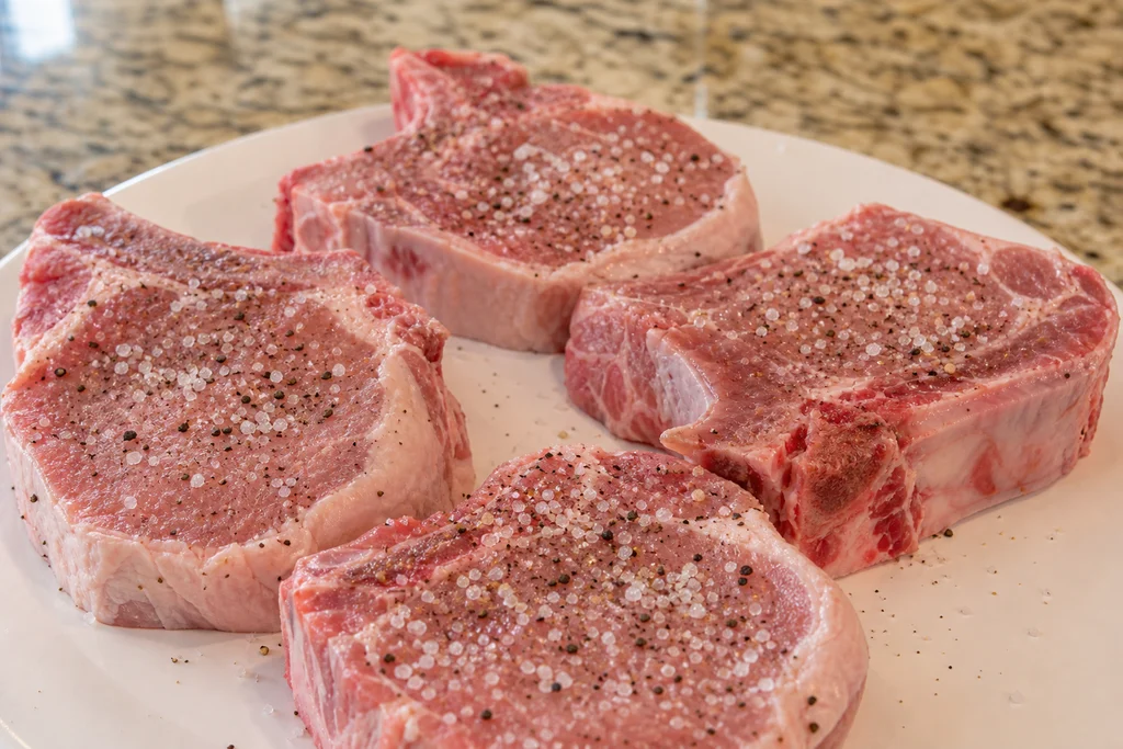 Seasoned raw bone-in pork chops with salt and pepper before searing