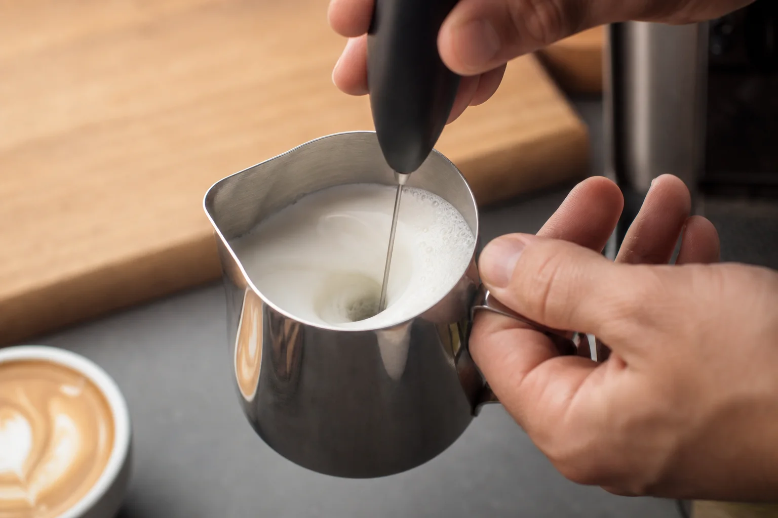 Milk being frothed with a handheld frother in a small pitcher for hojicha latte