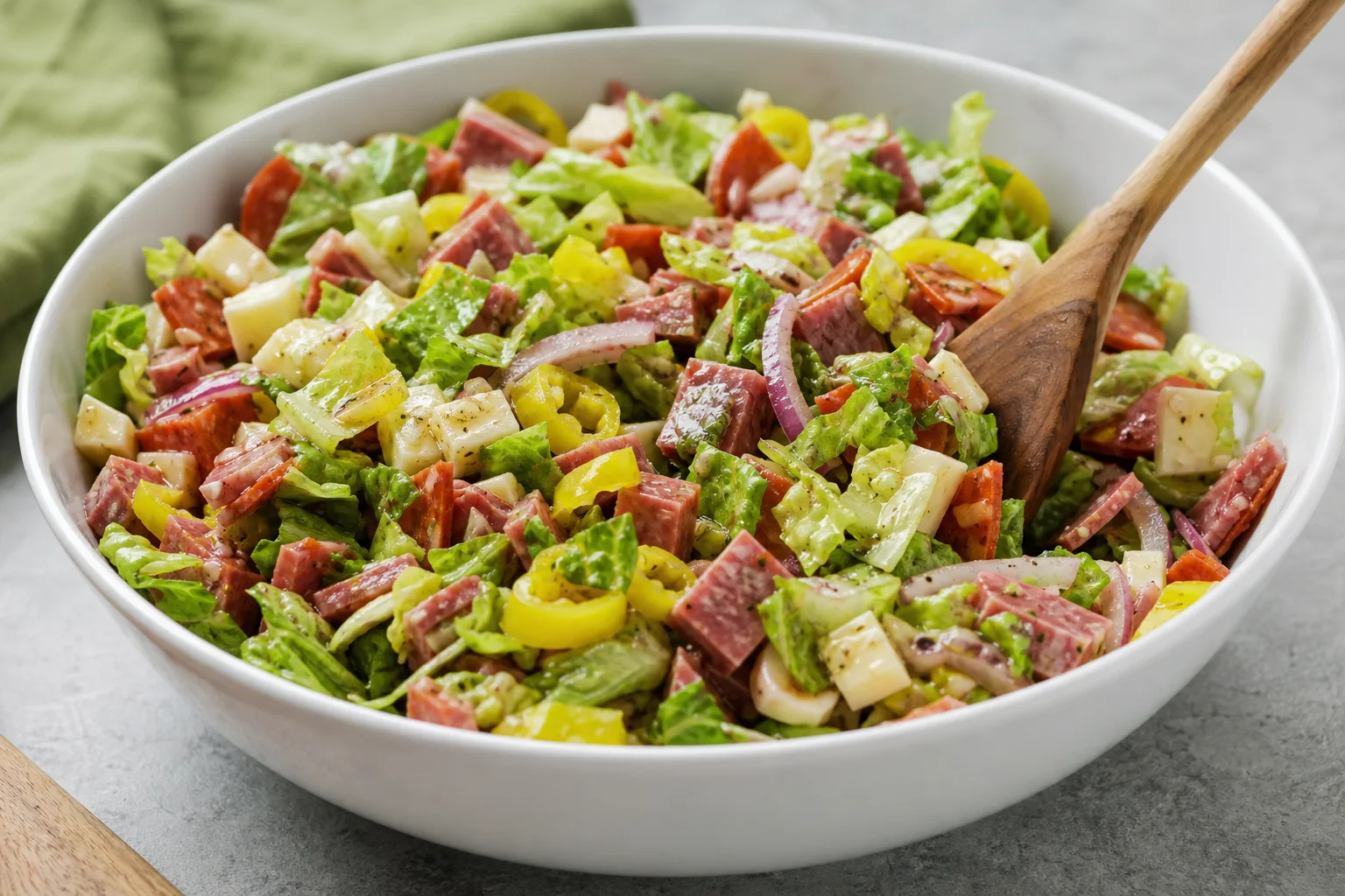 Chopped salami pepperoni provolone and lettuce tossed with Italian dressing in a large white mixing bowl