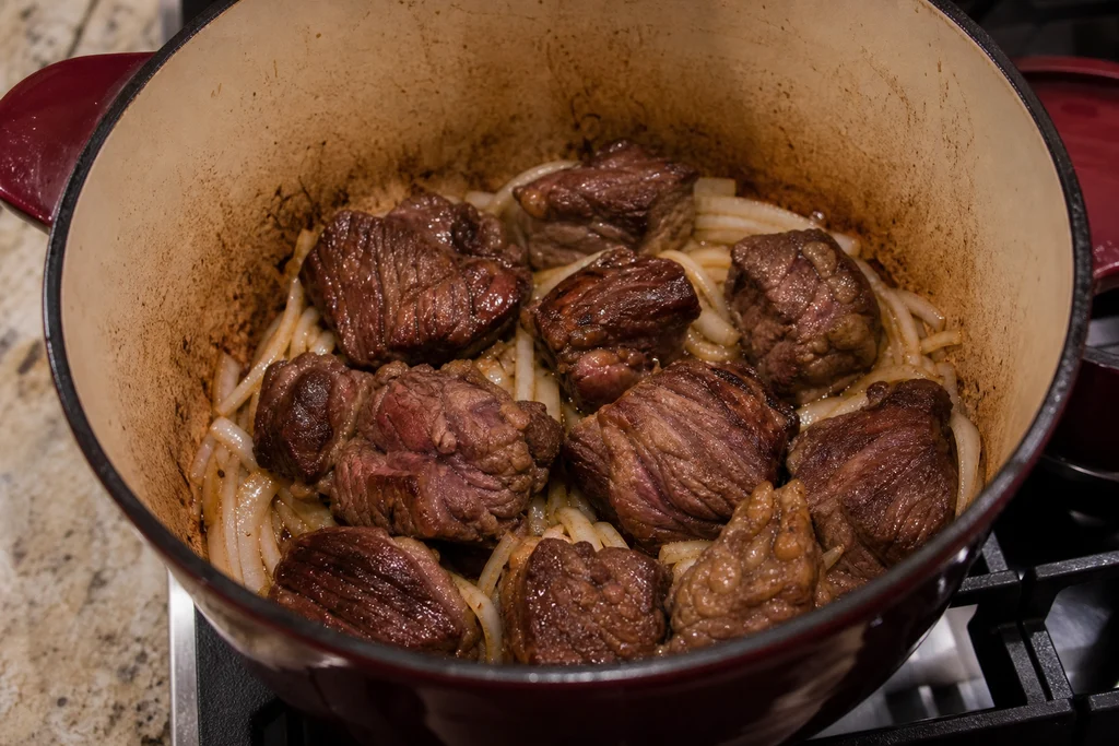 Searing beef chuck with onion for birria tacos in a Dutch oven