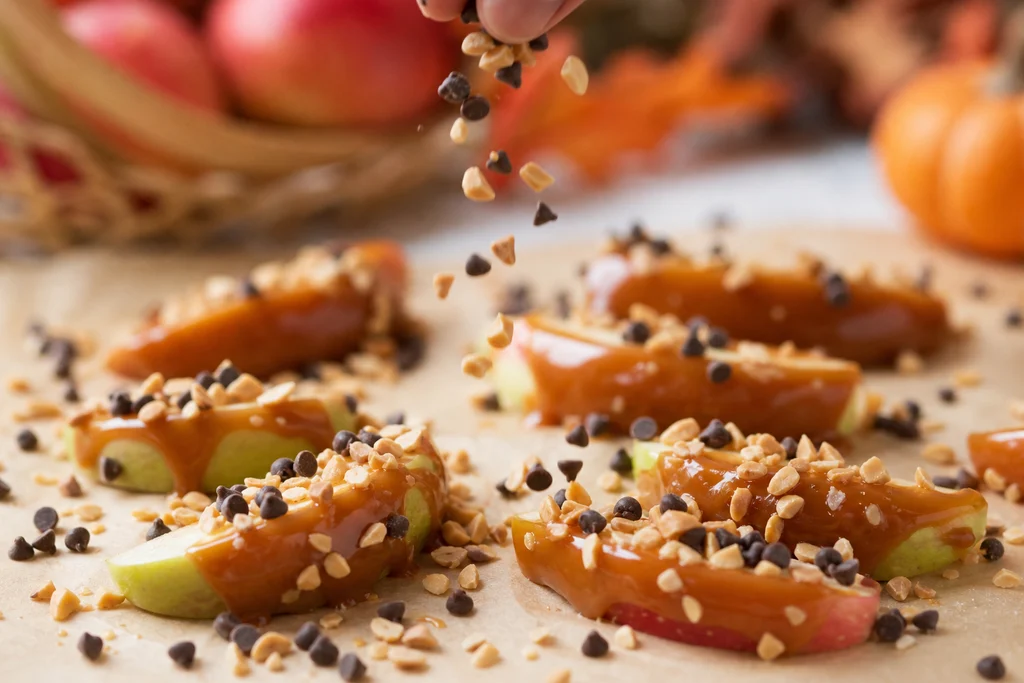 Sprinkling crushed nuts and chocolate chips on caramel apple slices