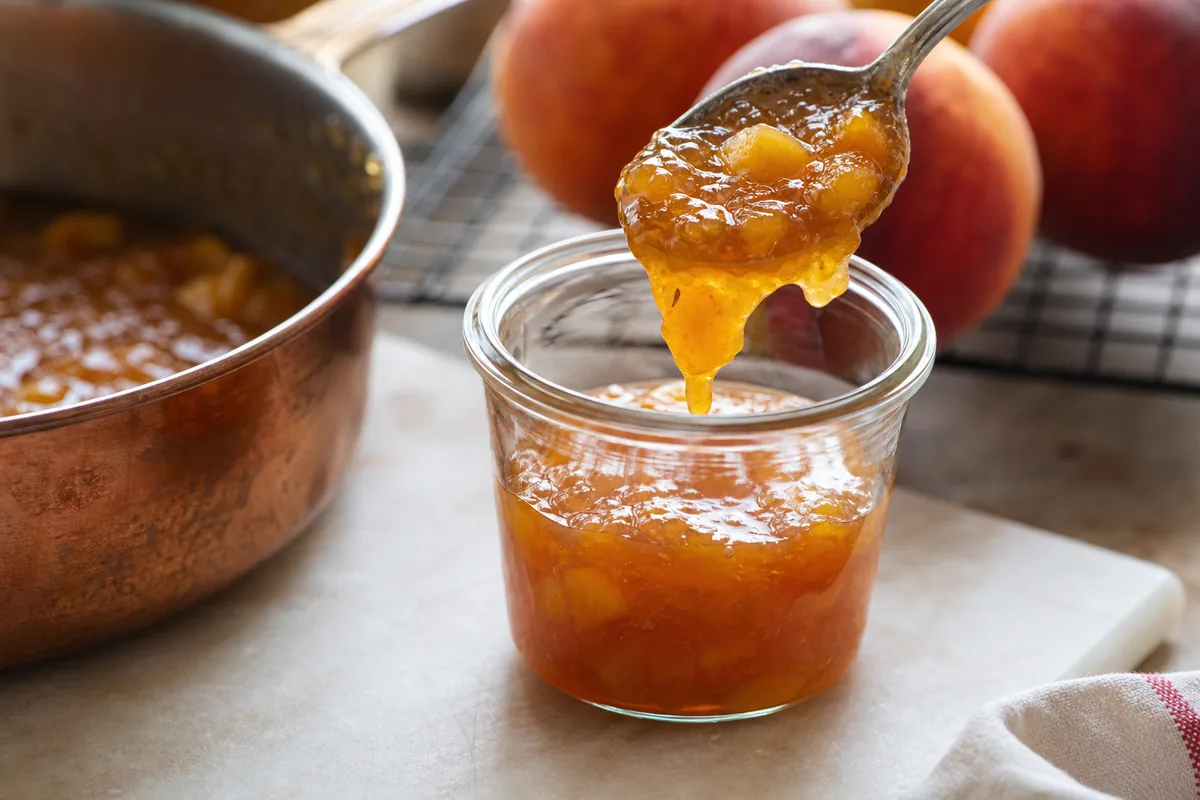 Warm peach jam being transferred into a clean refrigerator jar