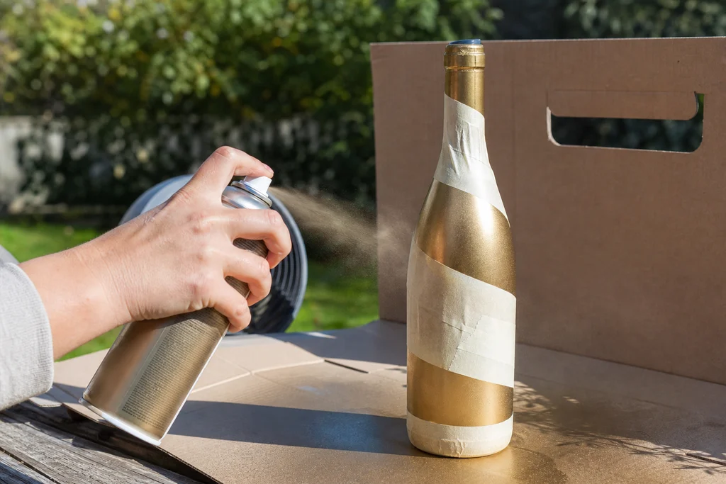 Spray painting a taped wine bottle outdoors for upcycled vase DIY