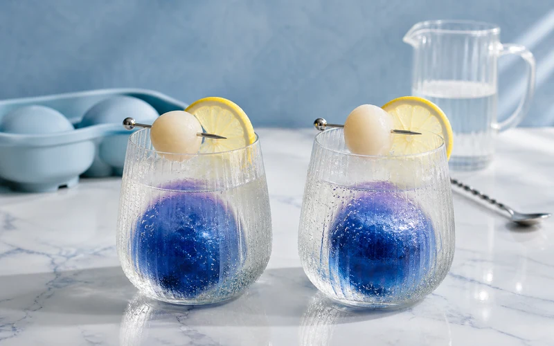 Two icy blue lychee mocktails with butterfly pea ice spheres