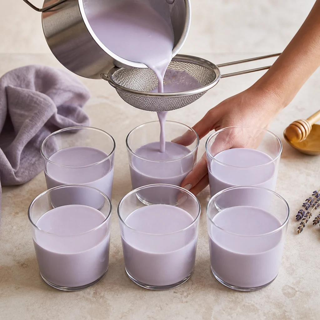 Strained pale lavender panna cotta poured into six identical glasses.